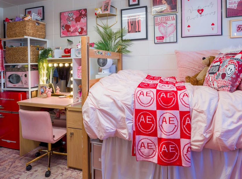 A cozy, well-organized dorm room with pink bedding, decorated walls, and a study area with a lit mir...