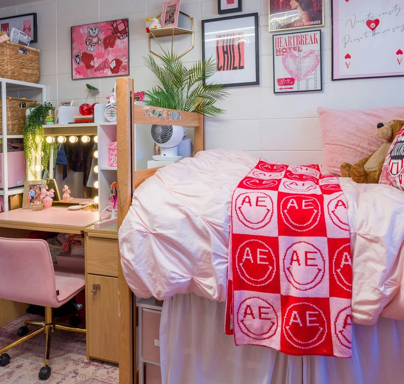 A cozy, well-organized dorm room with pink bedding, decorated walls, and a study area with a lit mir...