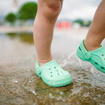 A child spashes through puddles wearing Crocs-style shoes.