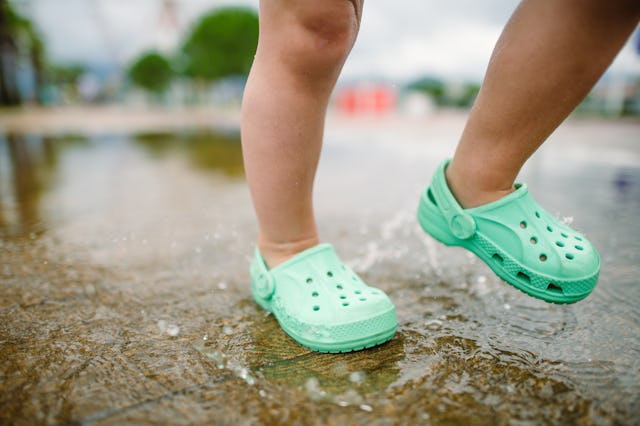 A child spashes through puddles wearing Crocs-style shoes.