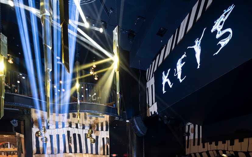Interior of a nightclub with blue lighting and beams, featuring a balcony labeled "KEYS" illuminated...