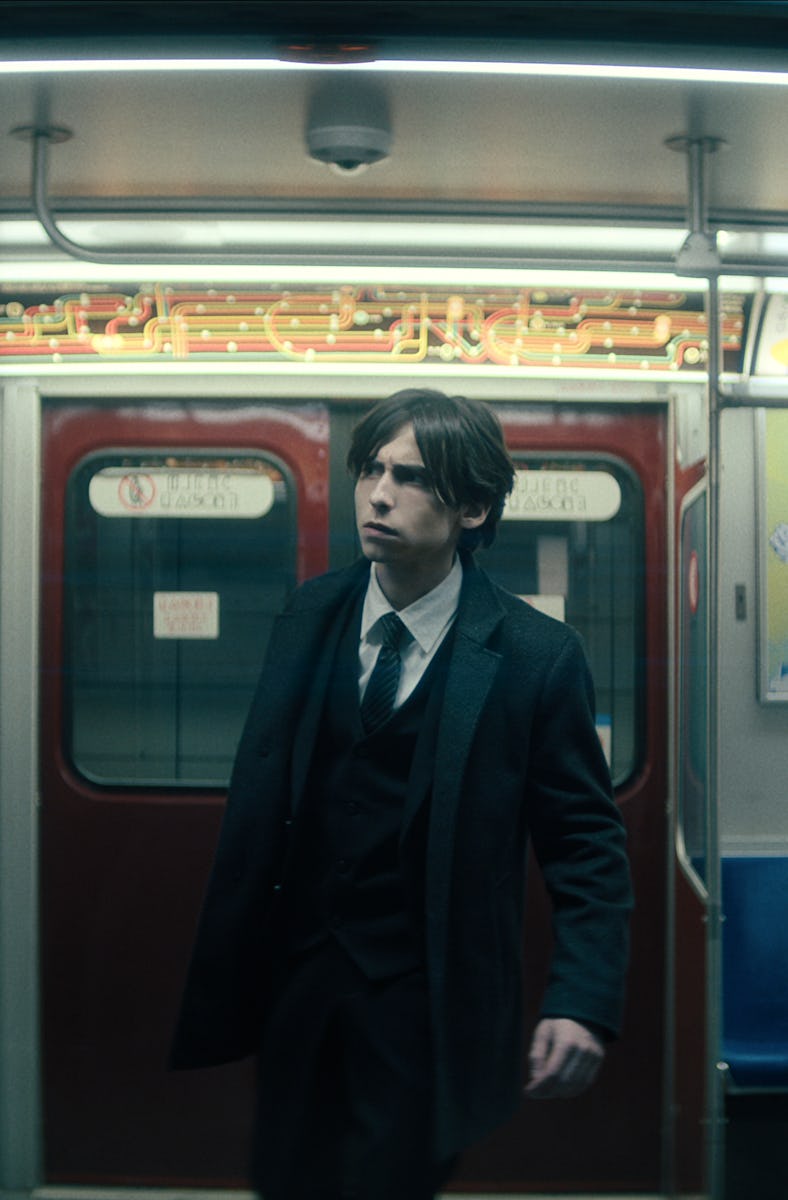 A man in a suit standing alone in a dimly lit subway train, appearing contemplative as he gazes towa...