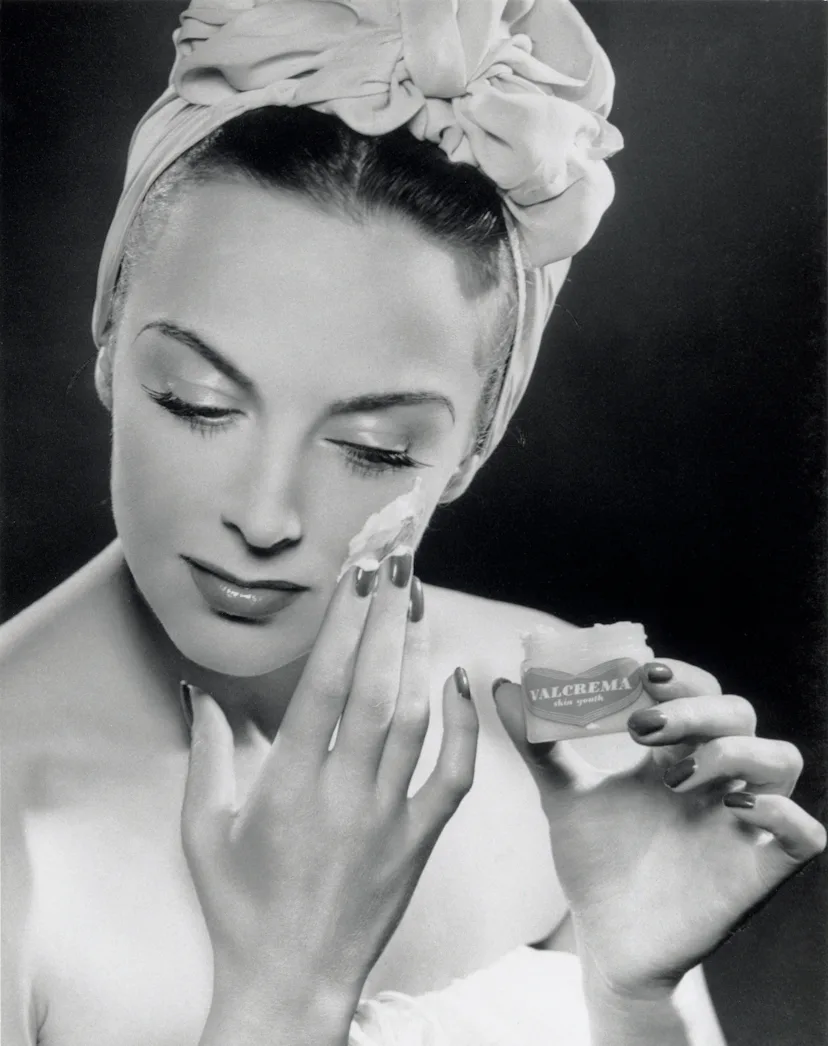 Woman applying skin cream, 1945-1955. Glamour fashion shot of a model applying Valcrema skin youth t...