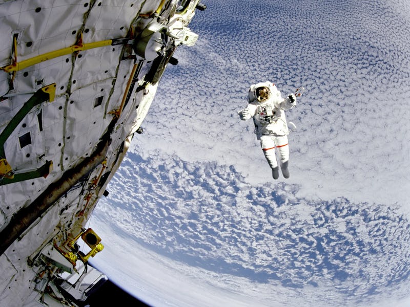 An astronaut, appearing anonymous since their helmet visor hides their face, reaches out towards the...