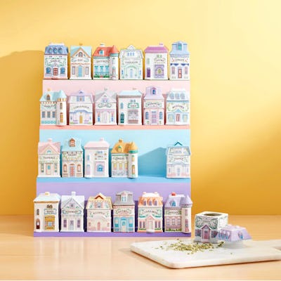 A colorful display of miniature ceramic houses on shelves, featuring intricate designs, with a cutting board and herbs in the foreground.