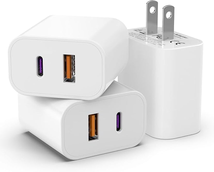 Three white charging adapters are stacked together, featuring USB-C and USB-A ports, with prongs for...