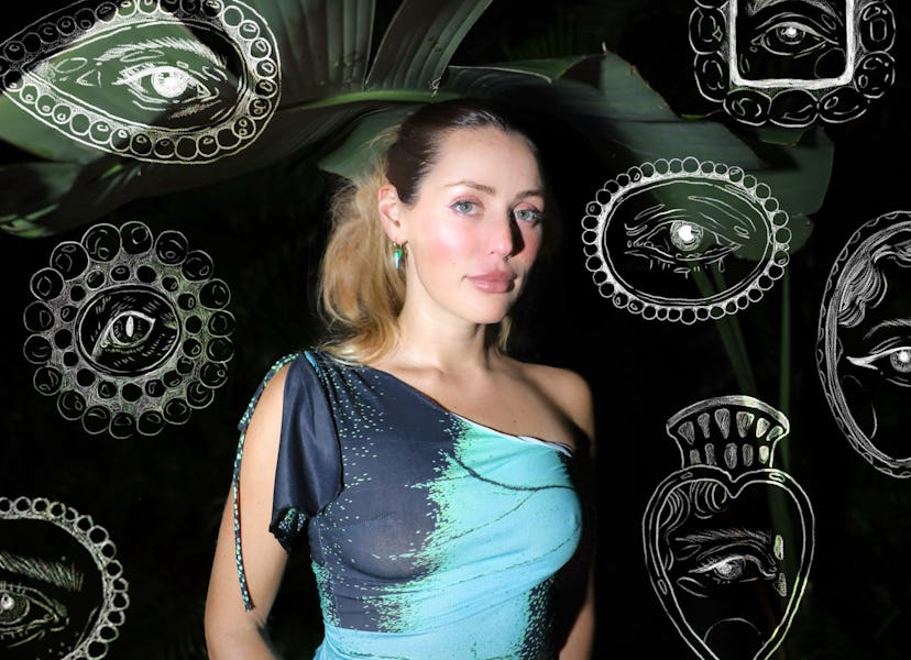 A woman stands in front of a dark background adorned with artistic illustrations of eyes, wearing a ...