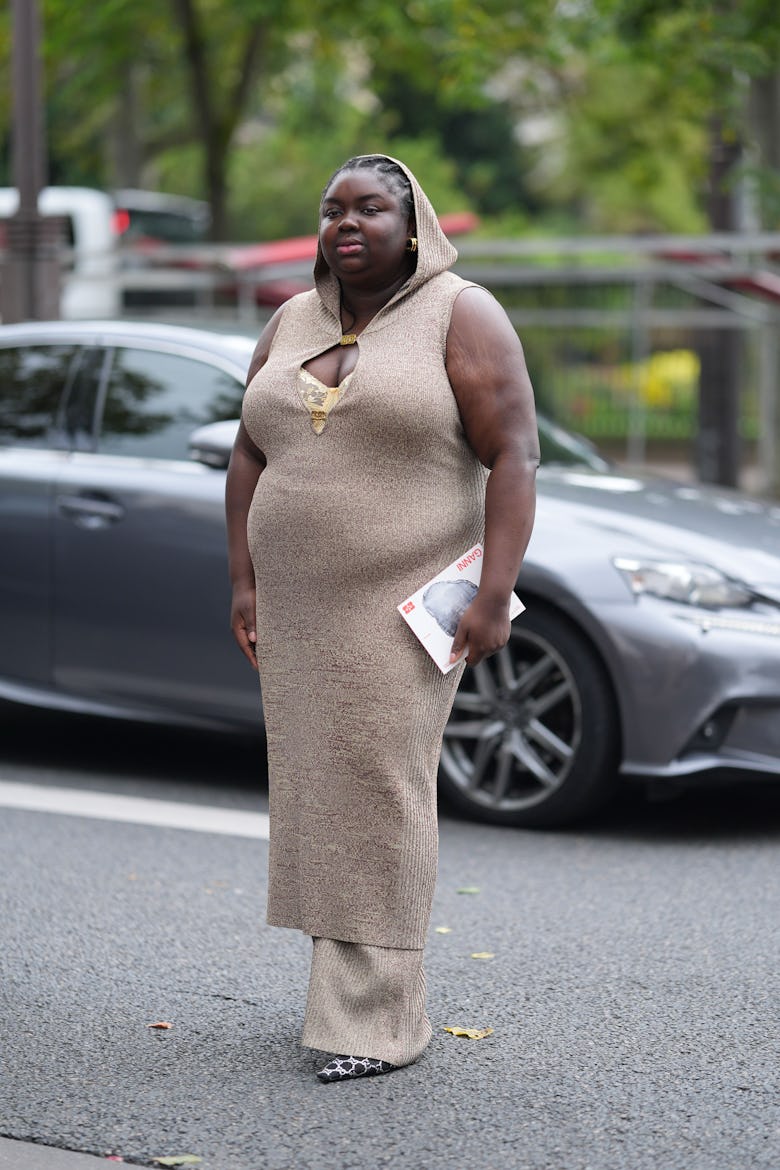 PARIS, FRANCE - SEPTEMBER 24: A guest wears gold earrings, light brown pattern hooded sleeveless cut...