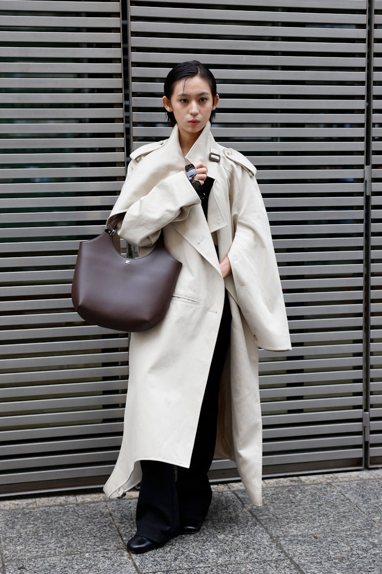 PARIS, FRANCE - SEPTEMBER 25: A guest wears beige trench coat, brown Courrèges bag, outside Courrège...