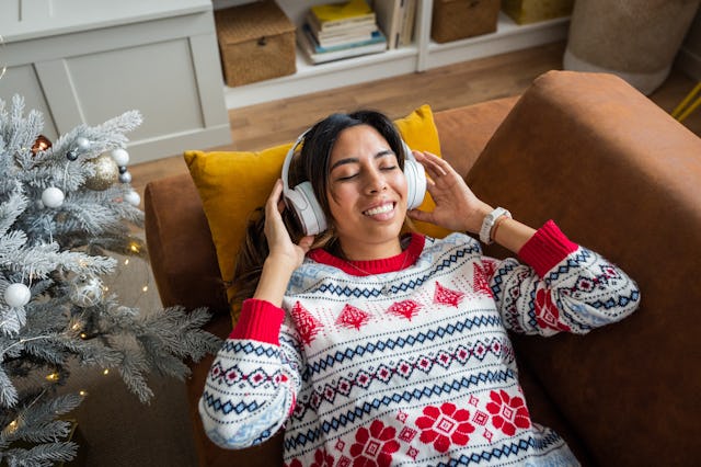 A woman relaxes on a couch, wearing headphones and enjoying music. She has a joyful expression and i...