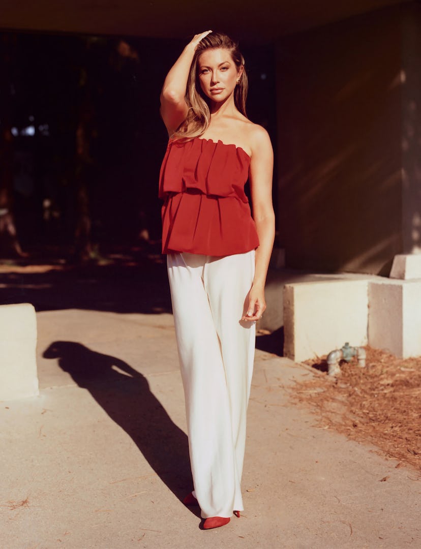 A woman stands confidently outdoors, wearing a stylish red strapless top and white wide-leg pants, w...