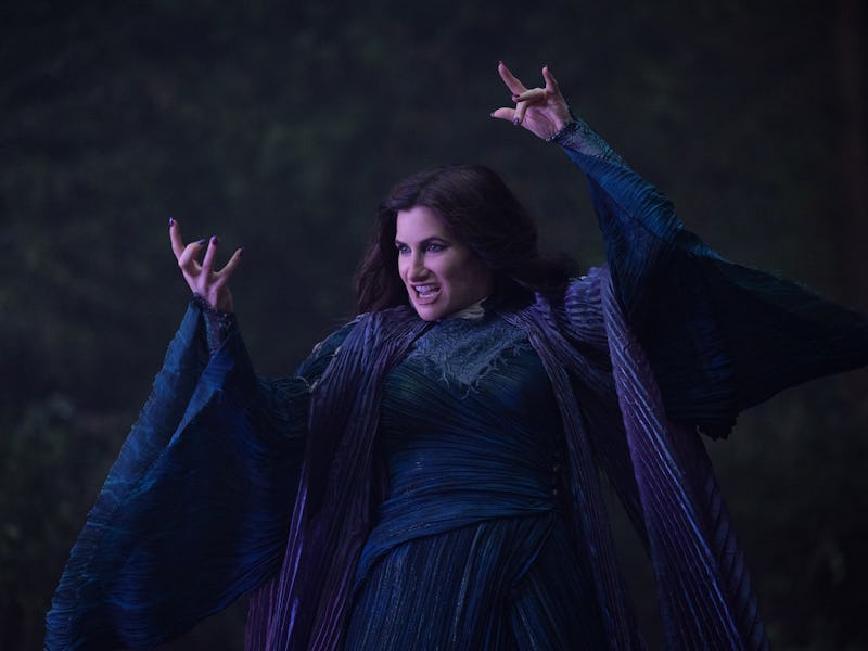 A woman in an ornate dark blue gown with flowing sleeves stands dramatically with outstretched arms ...