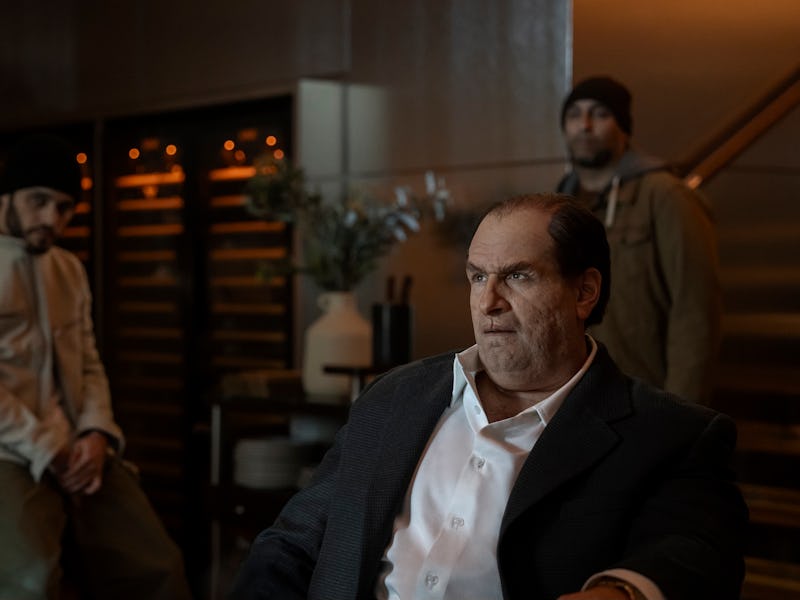 A tense scene in a stylish interior, featuring three men. One man sits in a suit, looking serious, w...