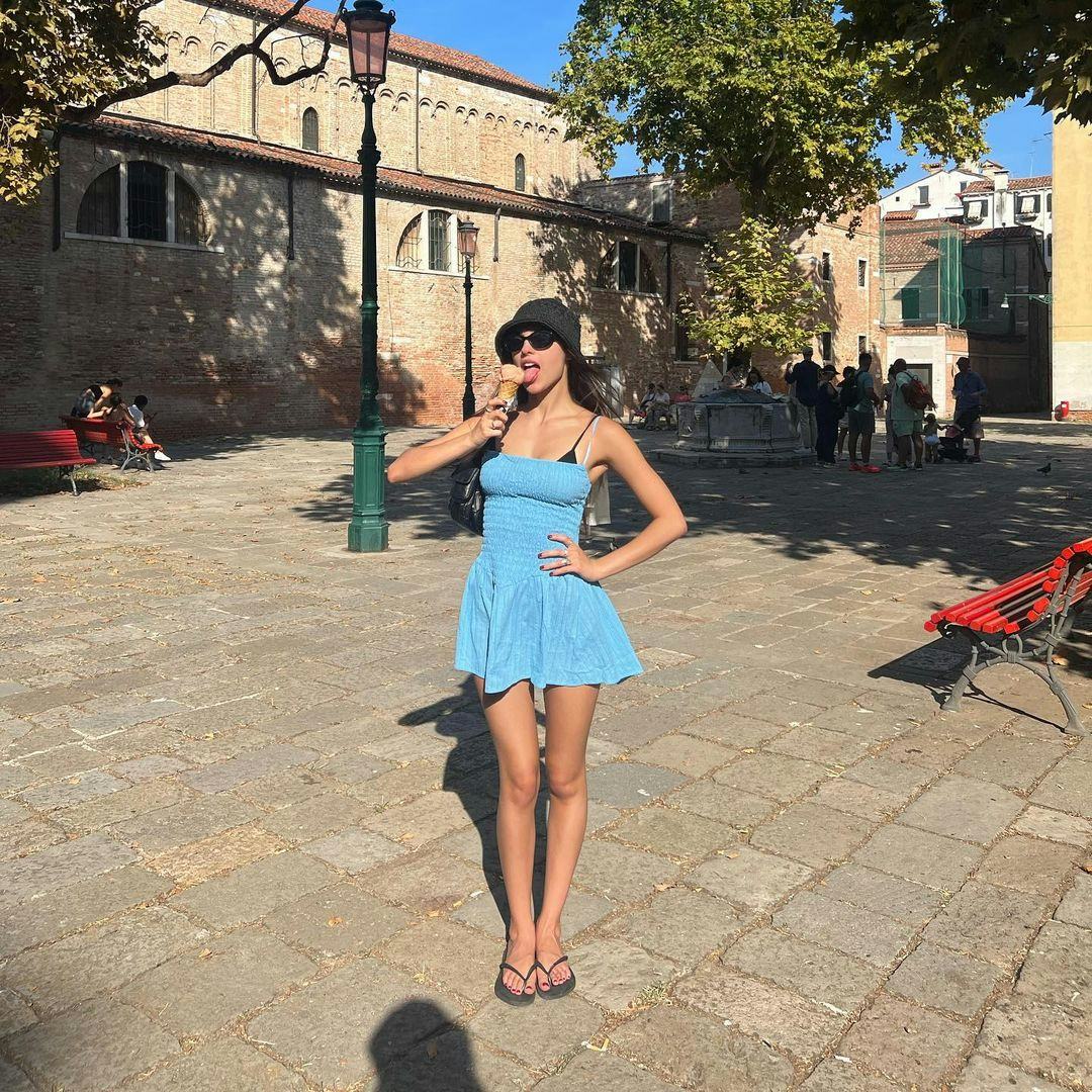 Olivia Rodrigo in Italy eating Gelato while wearing a blue dress and flip flops.
