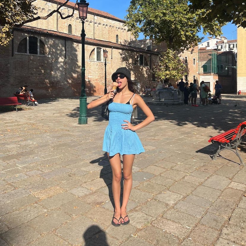Olivia Rodrigo in Italy eating Gelato while wearing a blue dress and flip flops.