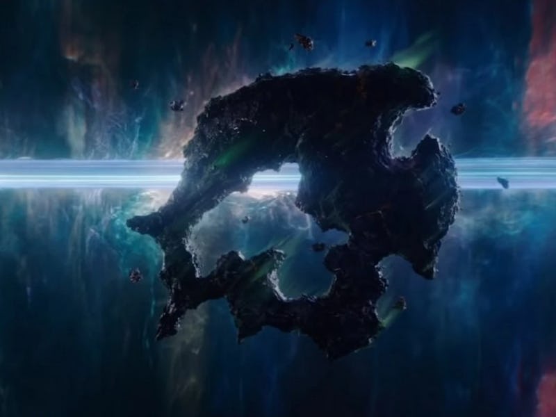 A dark, irregularly shaped object floats in a vibrant cosmic scene filled with swirling colors and g...