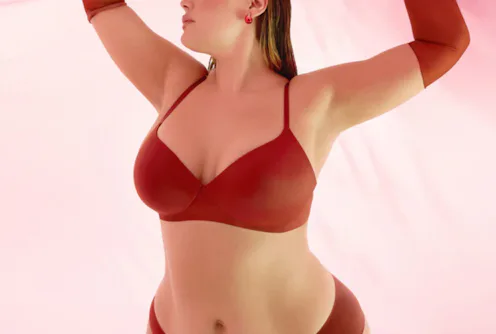 Model poses gracefully in a red bra and matching undies against a soft pink backdrop.