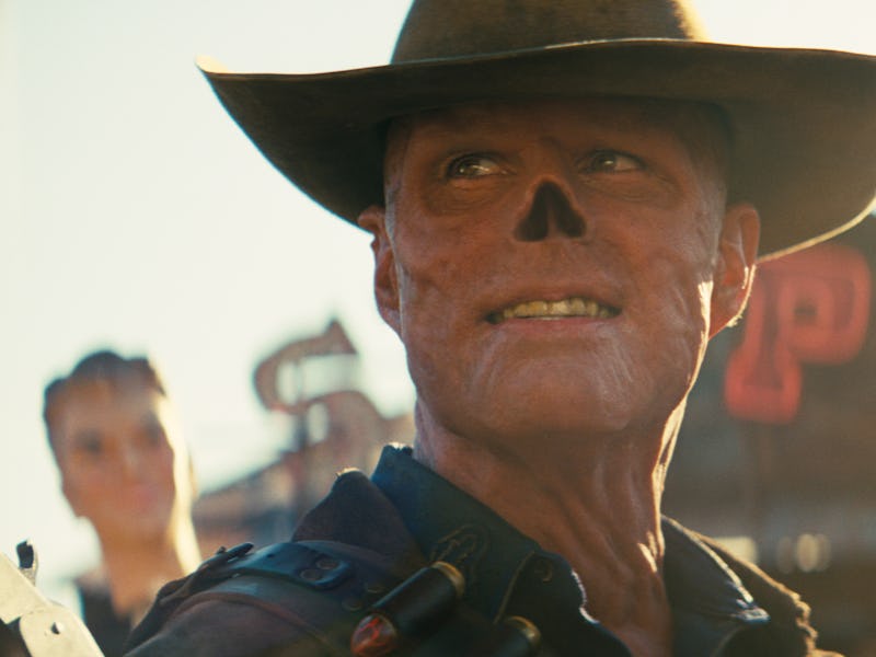 A man with a cowboy hat and a skull face makeup smiles confidently, set against a backdrop of a rust...