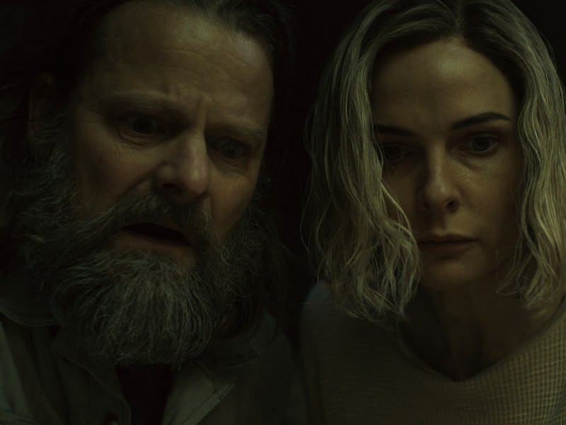 A man with a bushy beard and a woman with short, wavy hair lean forward, their faces illuminated wit...