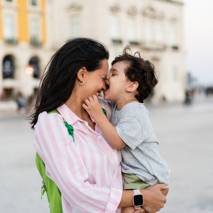 A smiling mother holds her young son close, sharing a joyful moment as he playfully pokes her nose, ...