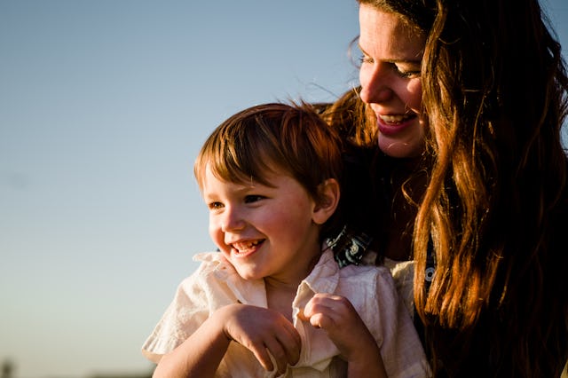 A woman and a young boy share a joyful moment outdoors, smiling at each other against a clear sky. T...