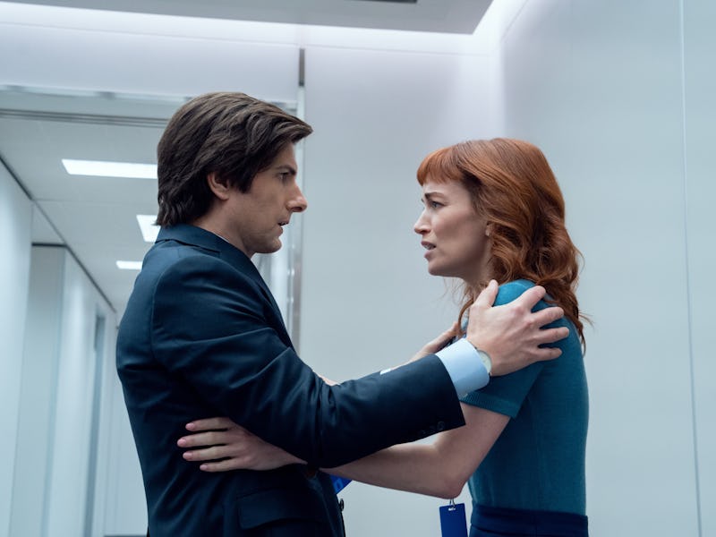 A man in a suit and a woman with red hair share an intense moment in a modern hallway, conveying str...