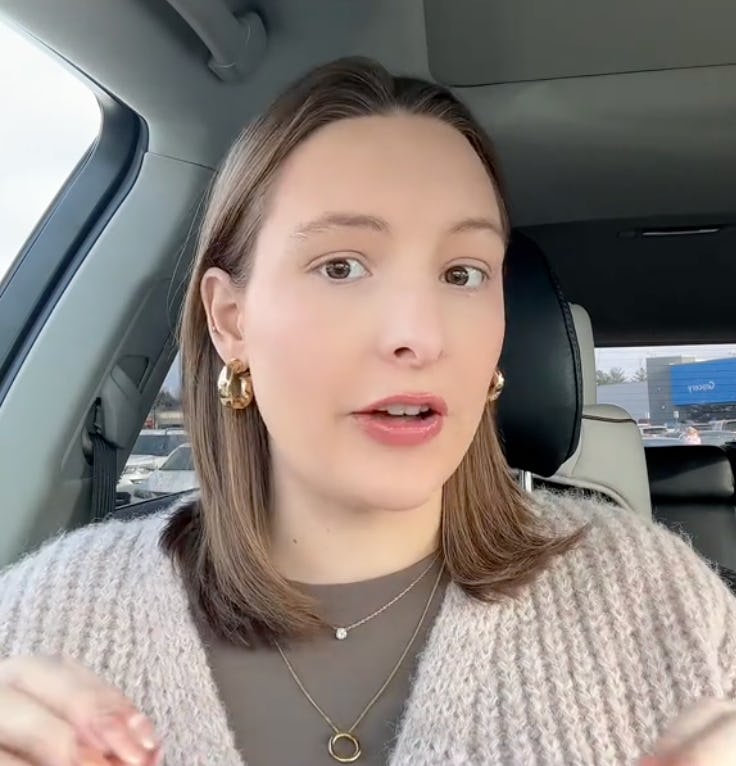 A woman with shoulder-length hair sits in a car, wearing a cozy sweater and gold hoop earrings, spea...