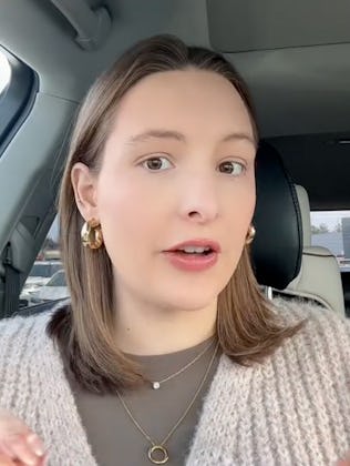 A woman with shoulder-length hair sits in a car, wearing a cozy sweater and gold hoop earrings, spea...