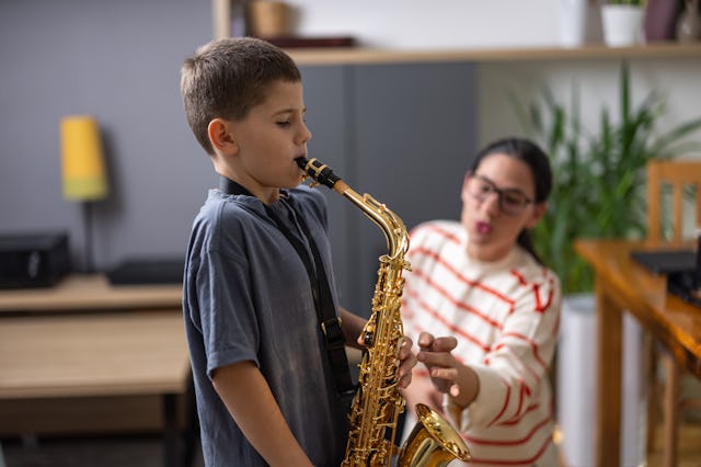 A young boy plays the saxophone attentively while a woman in a striped sweater offers encouragement ...