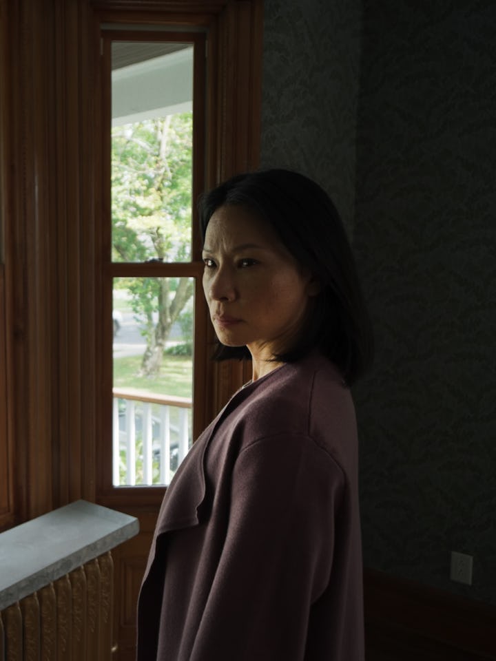 A woman stands by a window in a cozy room, gazing thoughtfully outside. Sunlight filters through the...