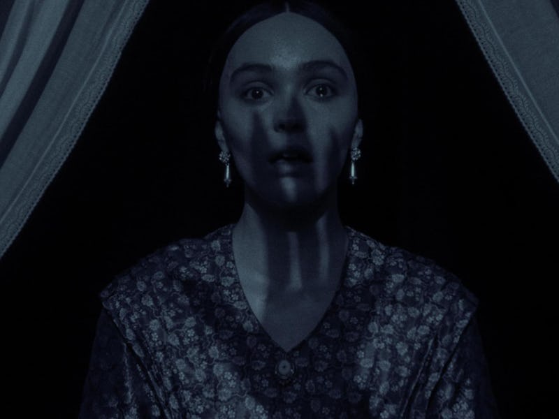 A woman sits in a dimly lit room, her expression one of fear or shock. Shadows cast across her face ...