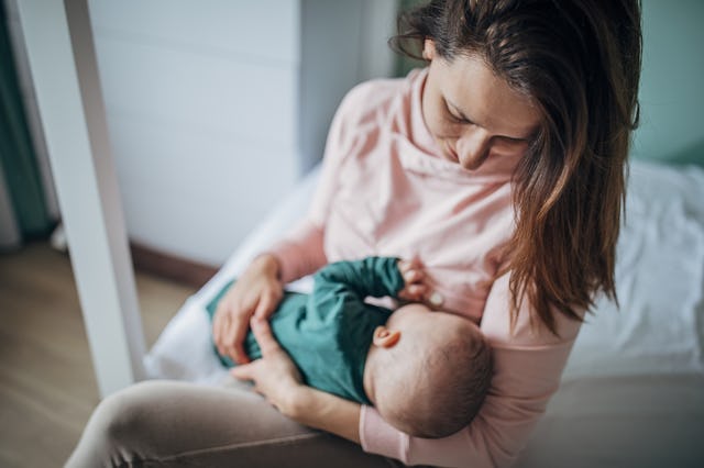 A mother gently breastfeeding her baby while seated in a softly lit room. She wears a pink top, and ...