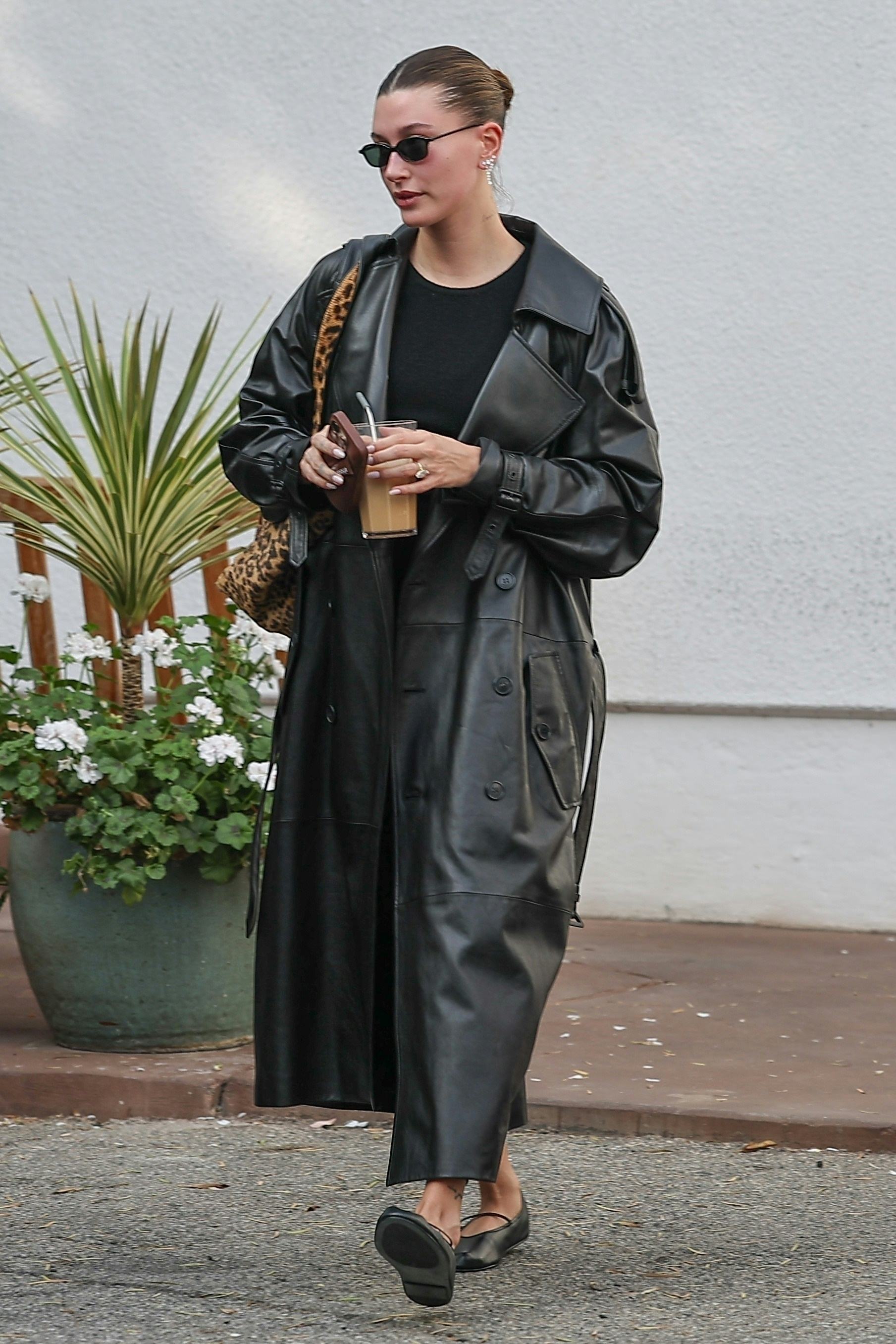 Hailey Bieber wears a black leather trench with leather shoes.