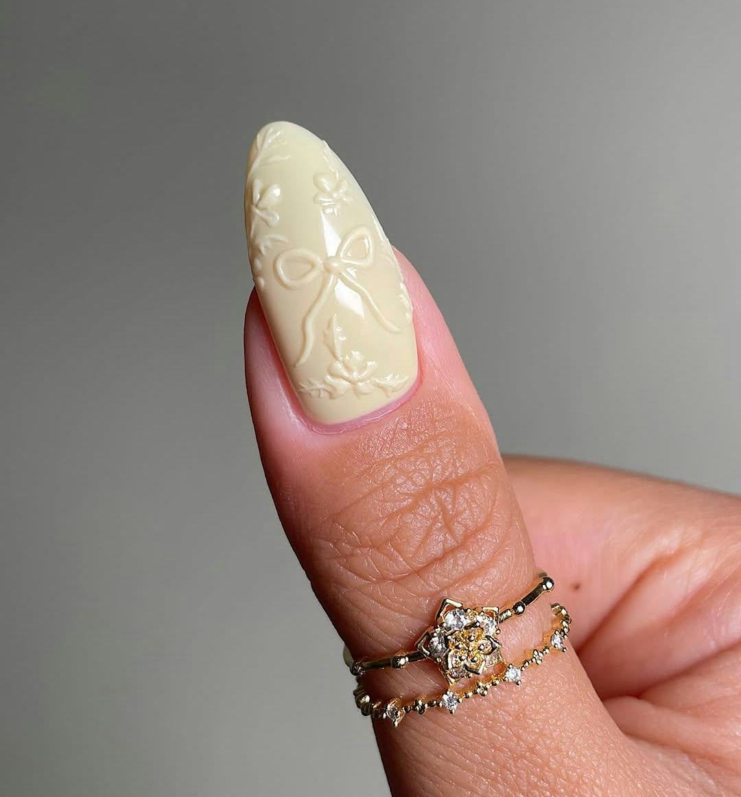 Butter yellow 3D ribbon nail designs match the 1960s aesthetic.