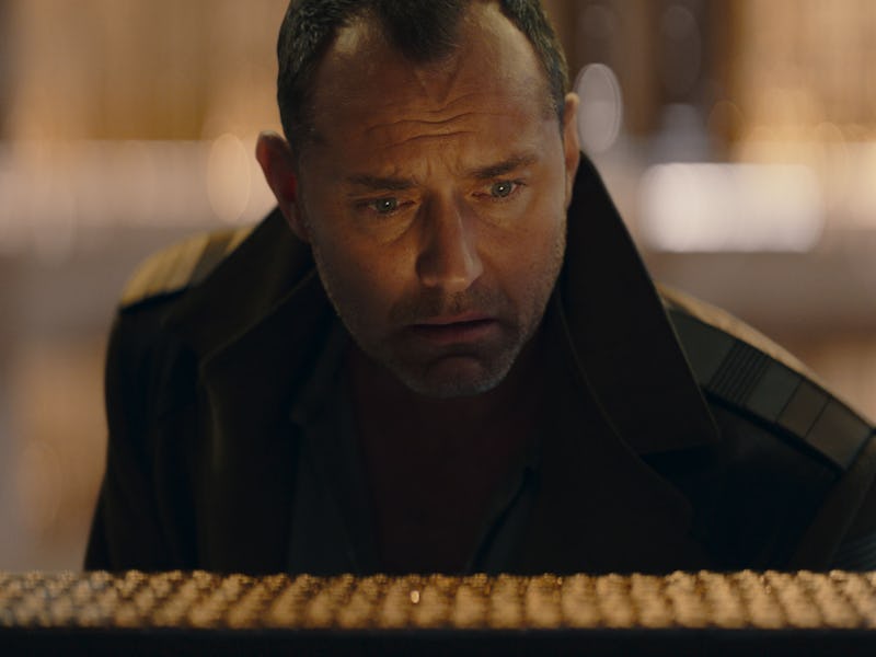 A man wearing a dark coat looks intently at a horizontal object in front of him, with a blurred, ill...
