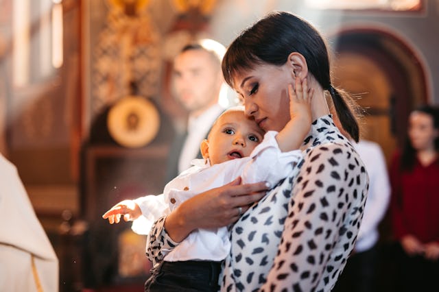 A woman holds a baby gently while looking at him lovingly. Soft light filters through the room, crea...