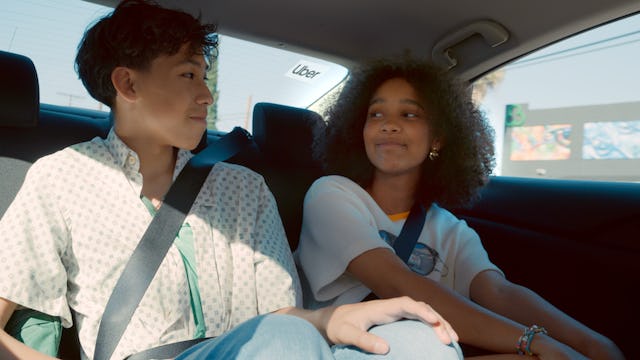 Two teens sitting in the back of an Uber, smiling at each other.