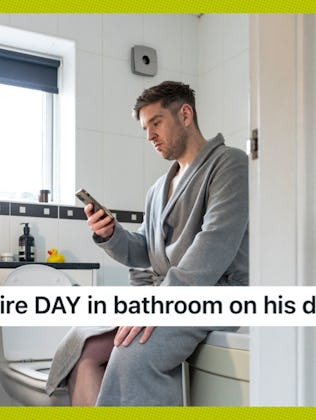 Man in a bathrobe sits on a toilet, looking at his phone. The bathroom has white tiles and a window ...