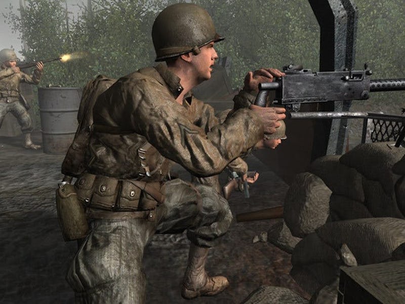 A soldier wearing a helmet and uniform operates a mounted machine gun behind sandbags, while another...