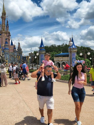 A crowd of people at a theme park, with a large castle in the background. Visitors are taking photos...