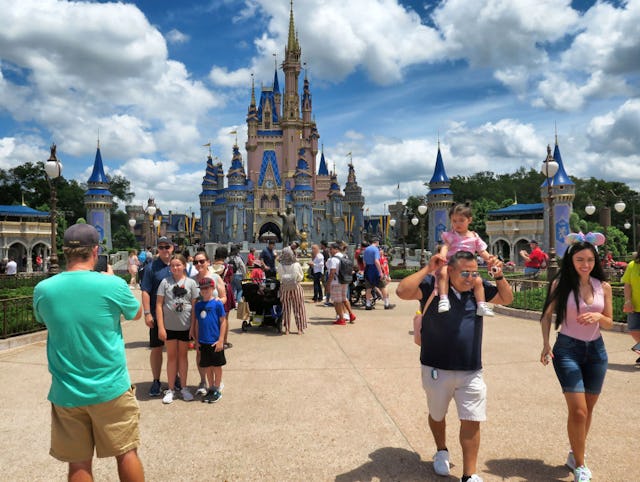 A crowd of people at a theme park, with a large castle in the background. Visitors are taking photos...