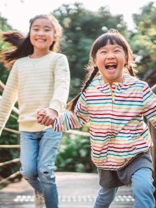 Two children, one in a striped jacket and the other in a striped sweater, joyfully run hand in hand ...