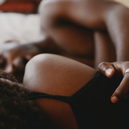 Two people lie closely on a bed, partially visible from shoulders up. One rests a hand on the other'...