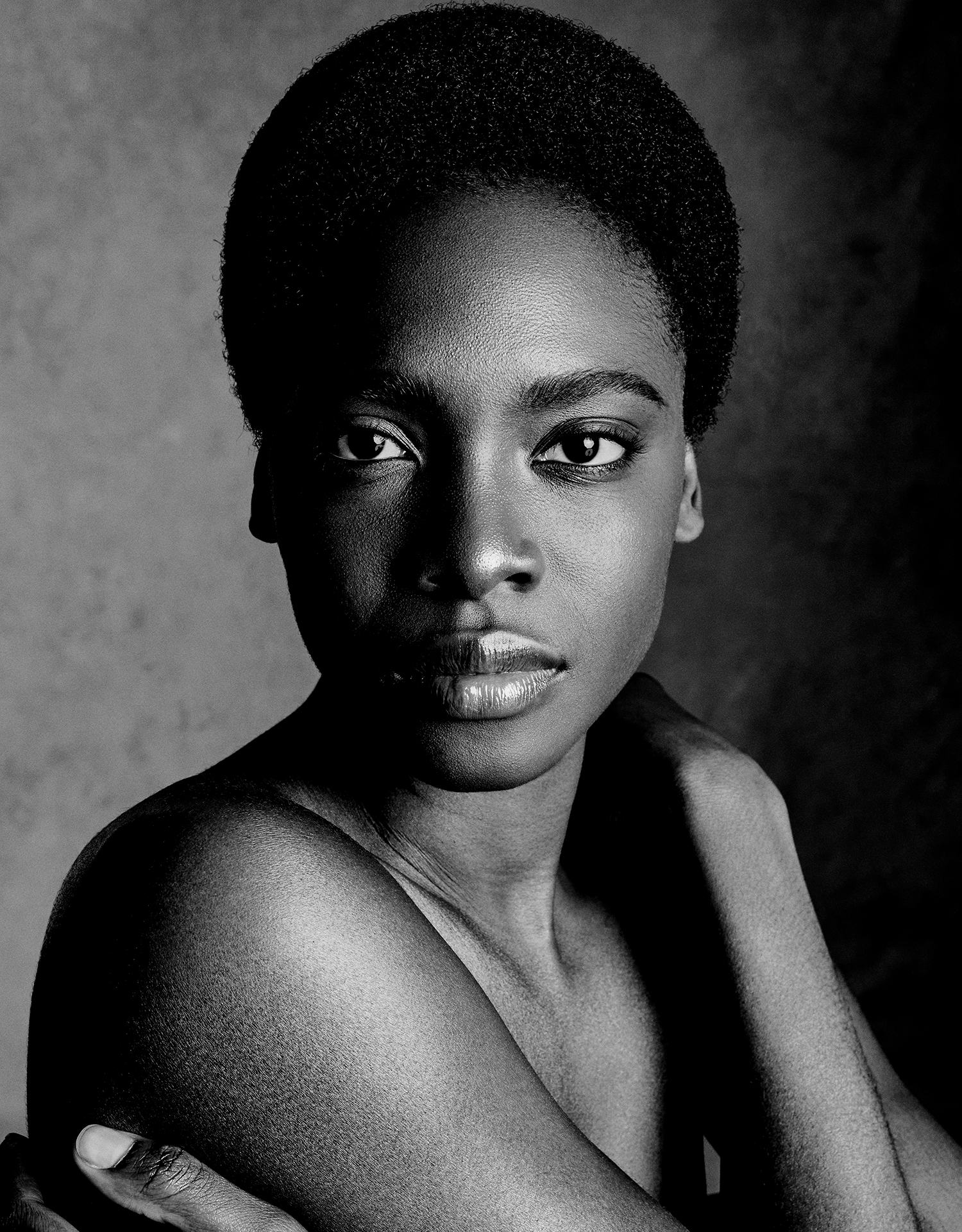 a model with short coily hair cropped close to their head, it's a beauty/glamour shot done in black ...