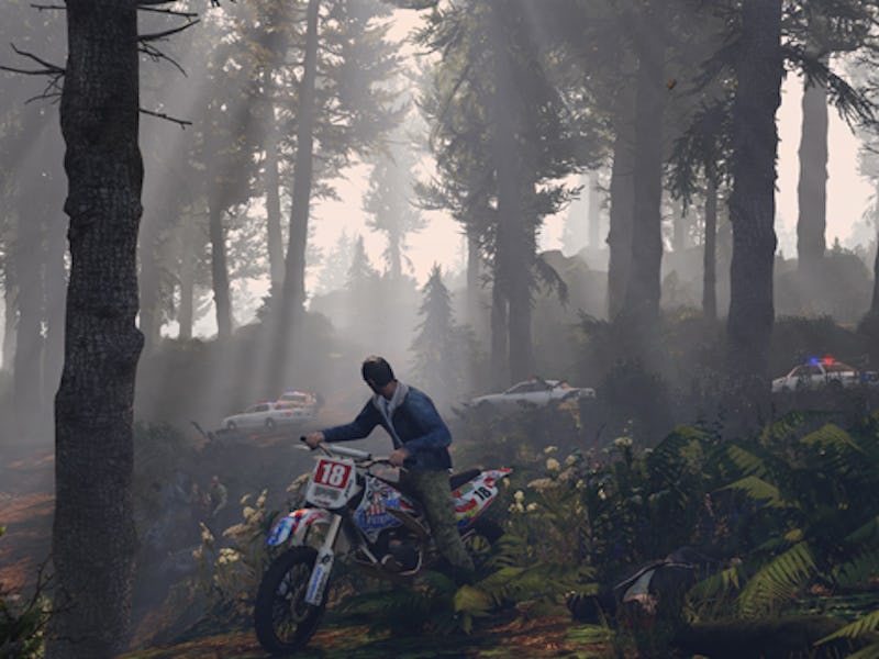 A motorcyclist navigates through a dense, sunlit forest. Several police cars are visible in the back...