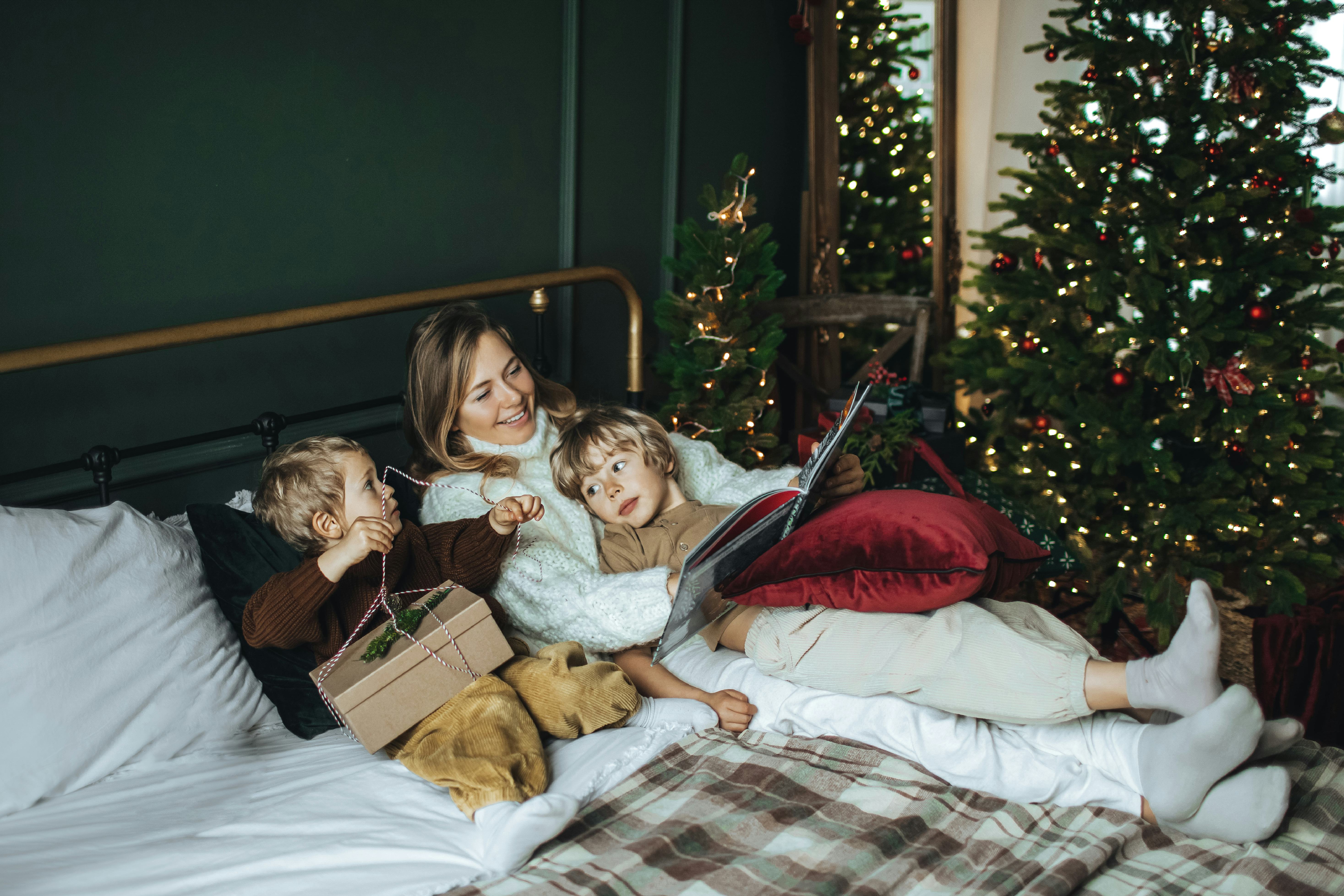 A mother and two children relax on a bed with a dog, surrounded by holiday decorations and Christmas...