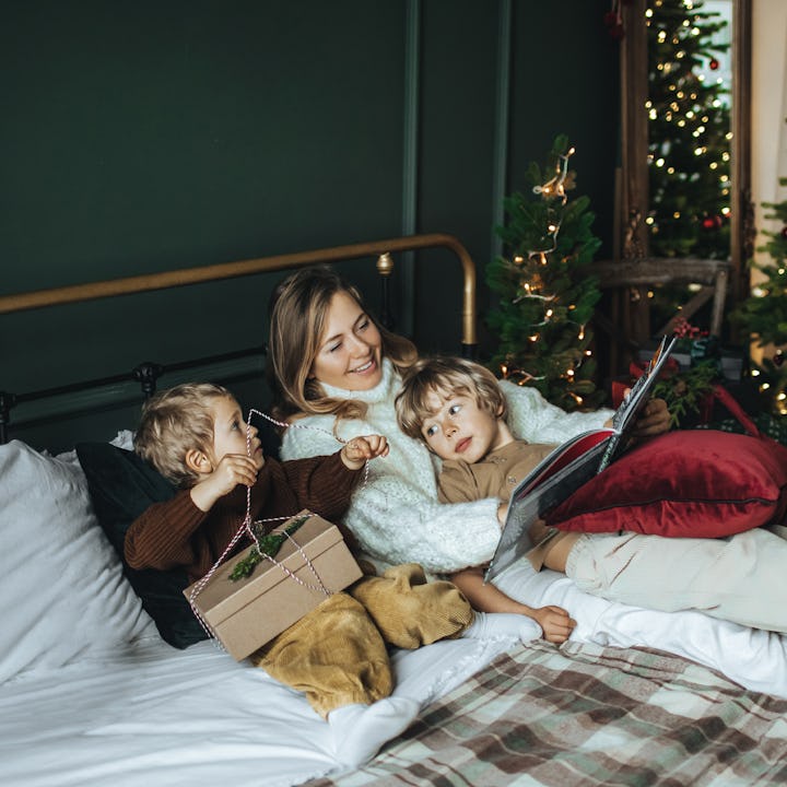 A mother and two children relax on a bed with a dog, surrounded by holiday decorations and Christmas...