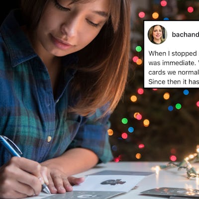A woman writes holiday cards in front of a Christmas tree.
