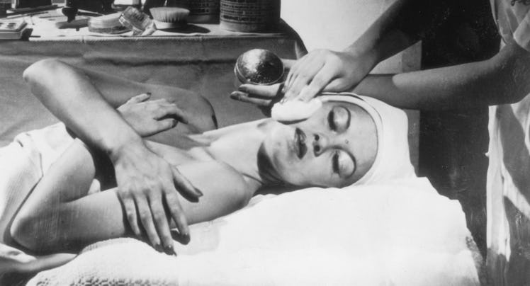 Three ghostly masks hang on the wall of a beauty parlour, where a woman is undergoing a facial treat...