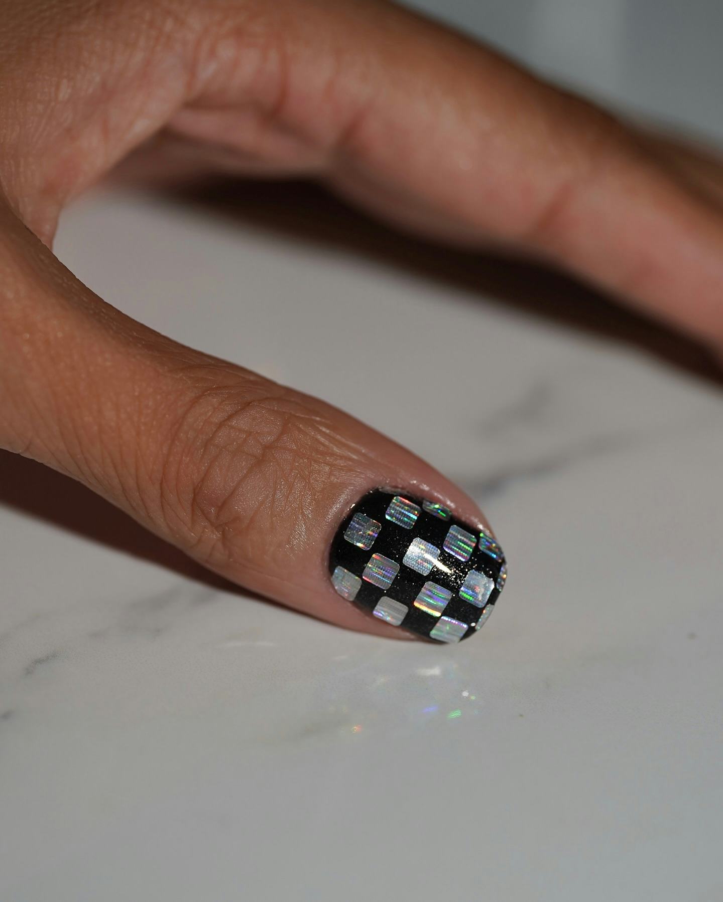 a thumb nail with black nail polish and a disco ball design with holographic squares 